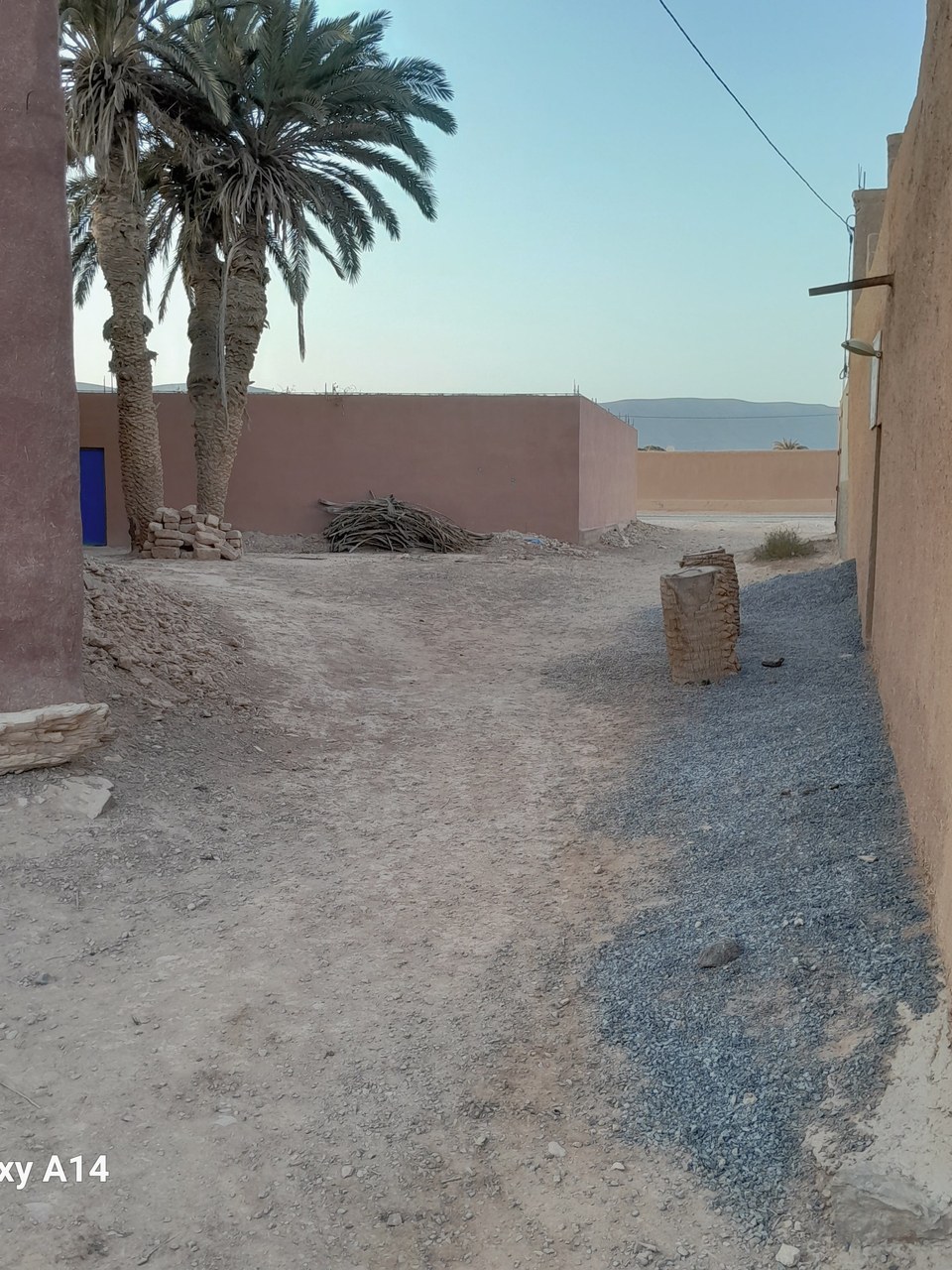 The earth-walled alley leading down to the road, with Firm Foundations on the left.